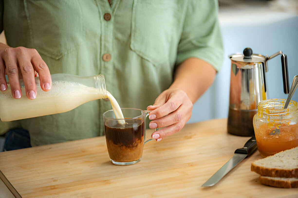 Woman pouring vegan milk into a cup of black coffee. Soy milk, oat milk, almond milk Woman pouring vegan milk into a cup of black coffee. Soy milk, oat milk, almond milk